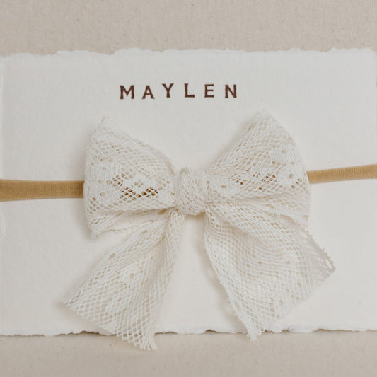 White lace bow on a beige headband with 'MAYLEN' branding on a white background