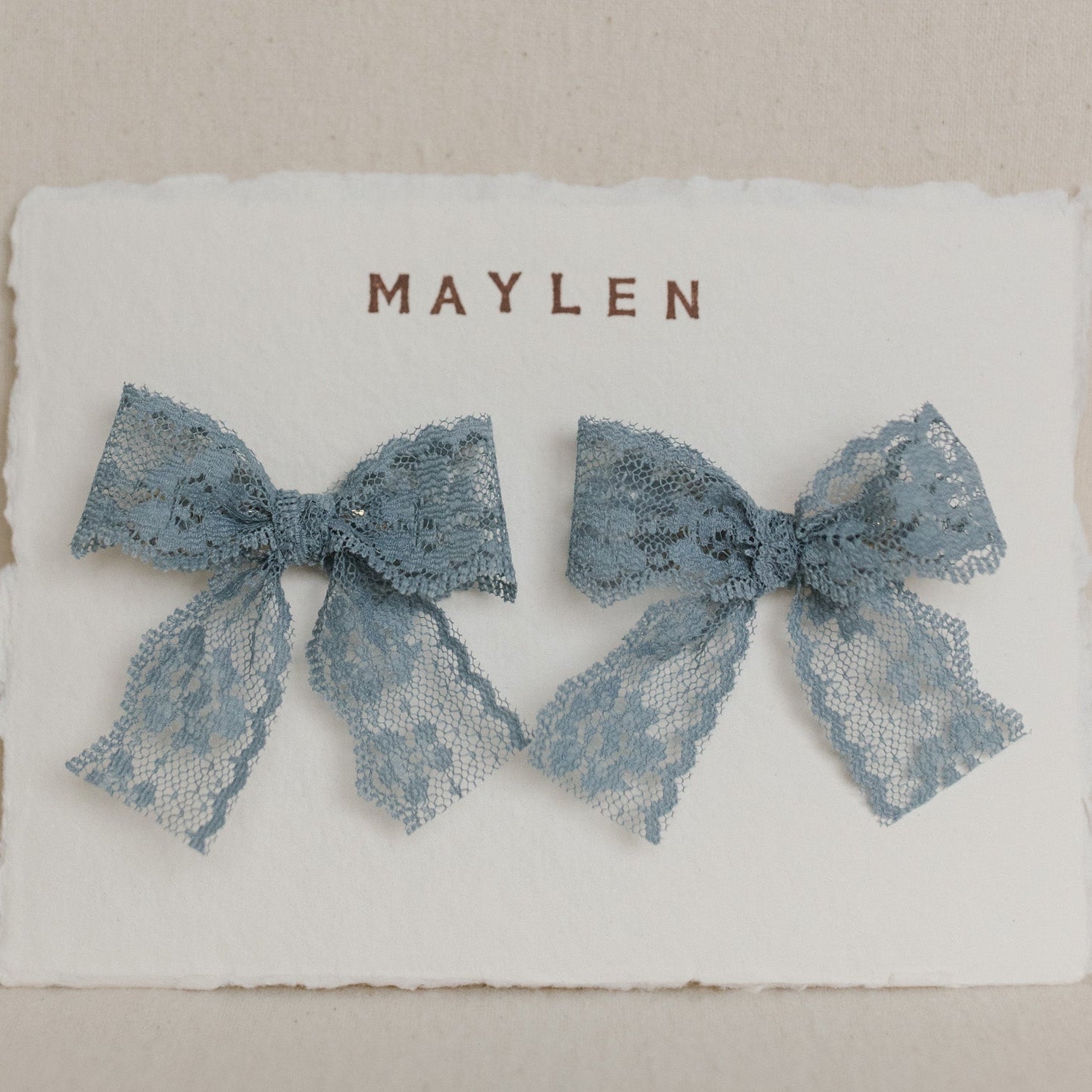 Two blue lace bows on a white card with 'MAYLEN' printed on it.