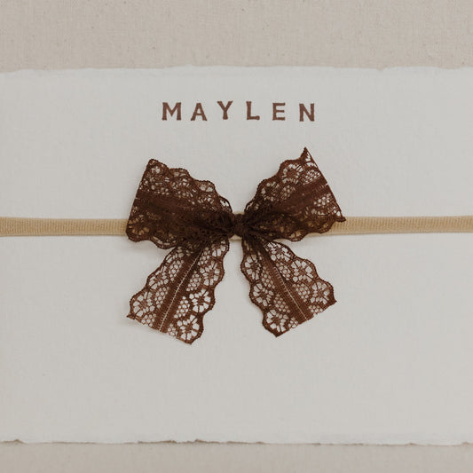 White card with a brown lace bow and 'MAYLEN' text on a beige background