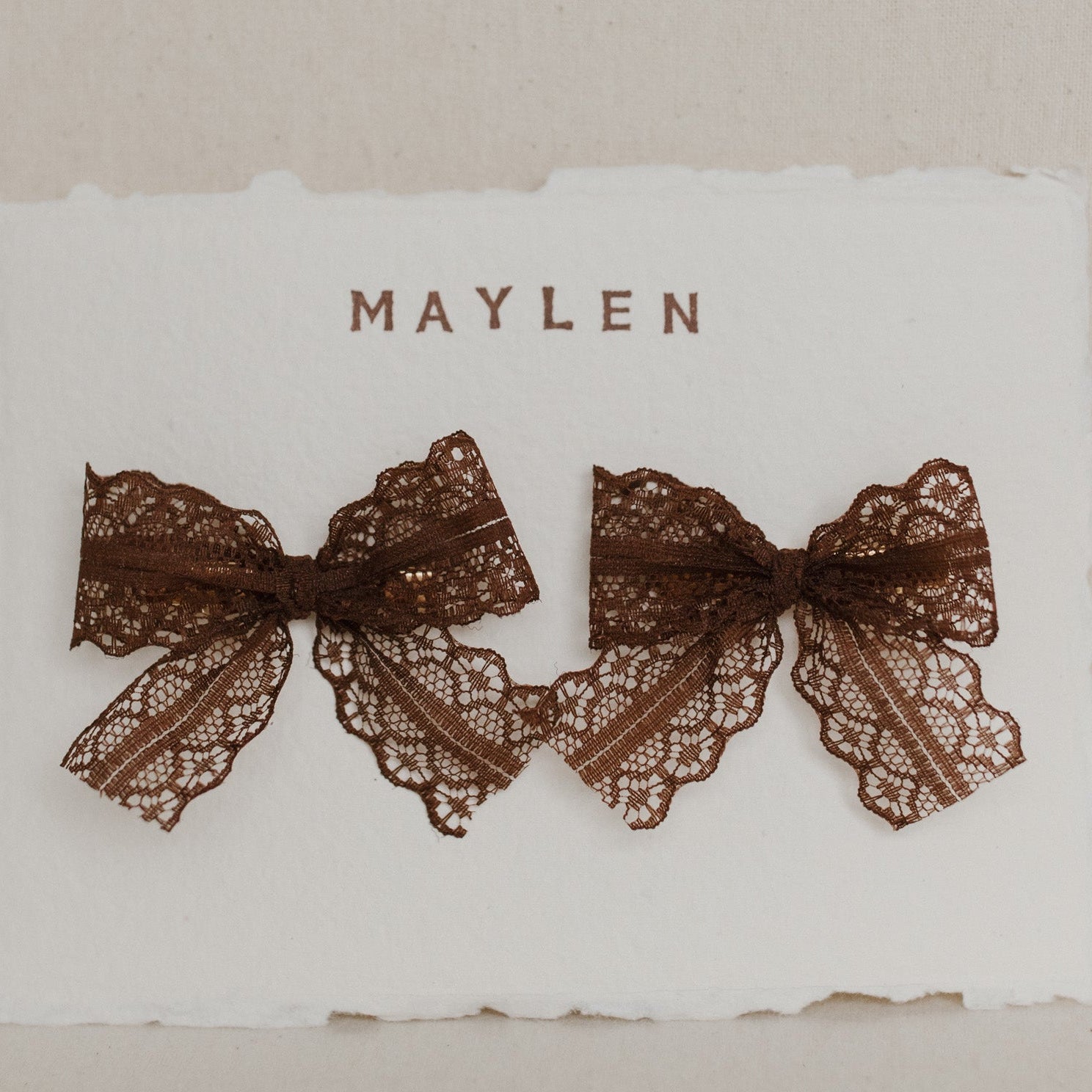 Two brown lace bows on a white card with 'Maylen' branding.